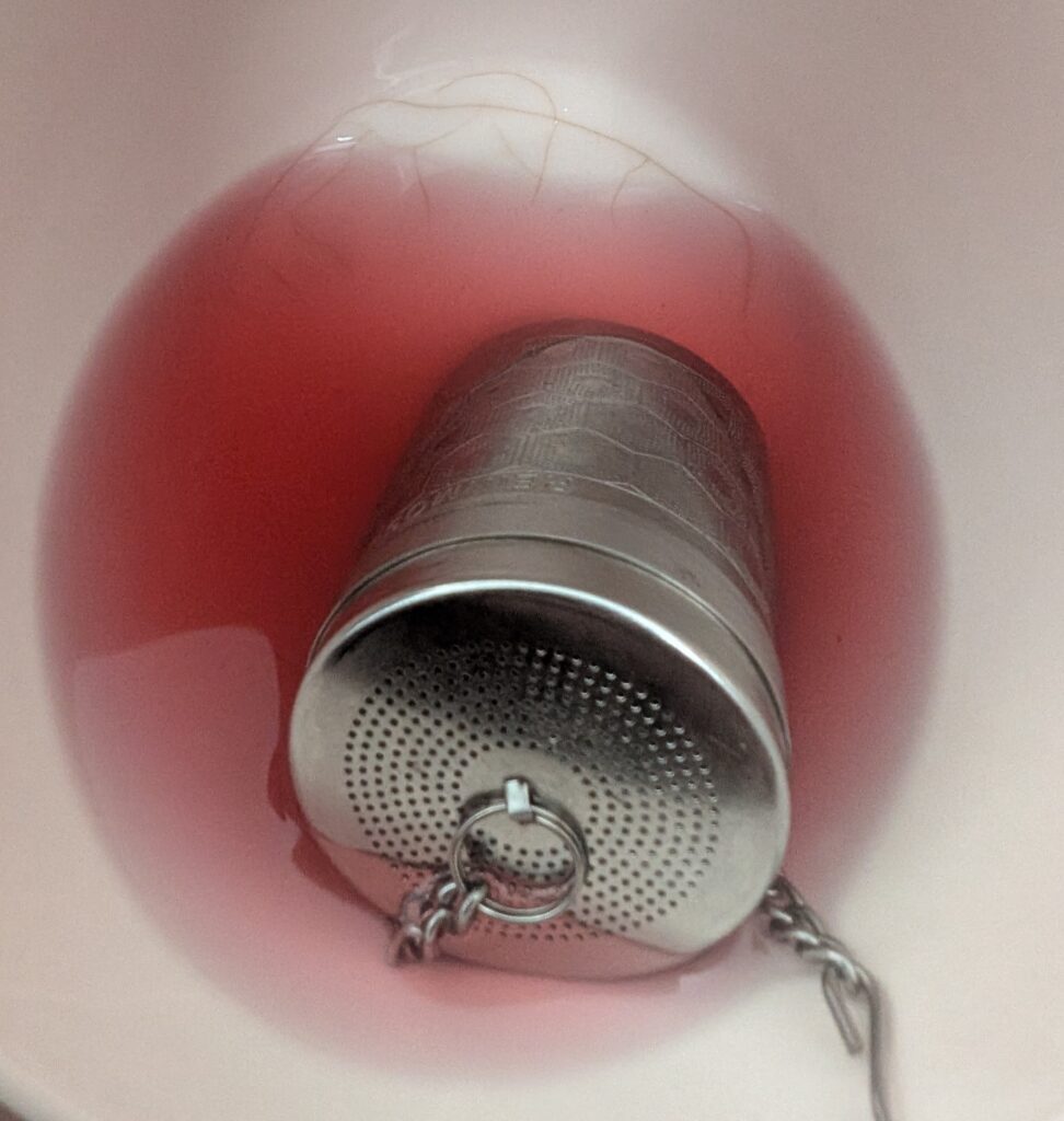 Deep red roselle tea in a cup brewed from dried roselle calyx in a tea strainer.